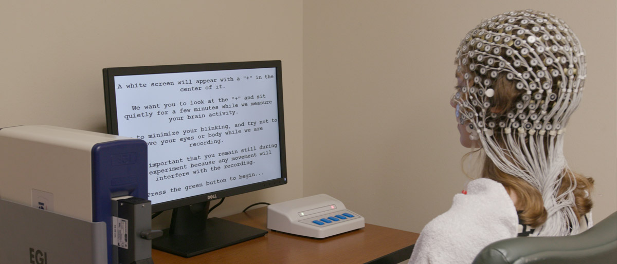 Woman sitting in front of screen with electrodes attached to head