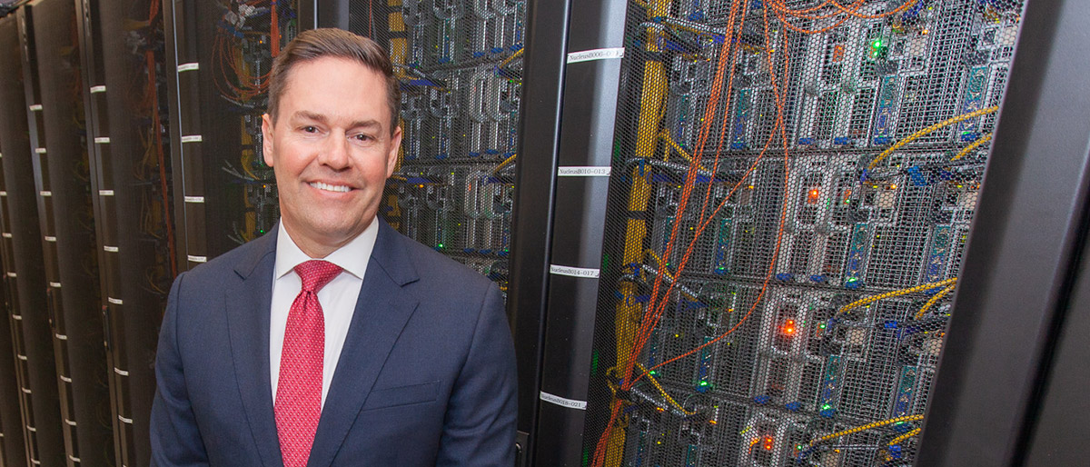 Man in suit standing in front of server racks, mesh cabinets with wires