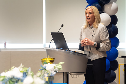 Woman standing in front of a column of balloons speaks from a podium.