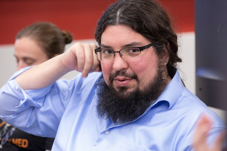 Man with glasses and a beard looking at talking teammate