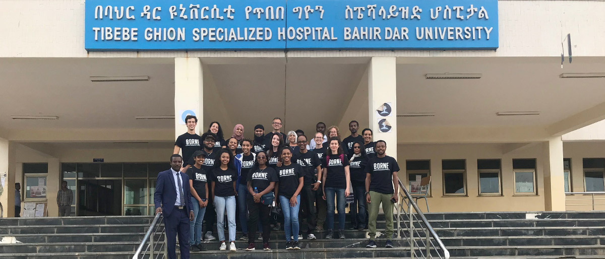 Group of people in black shirts standing in front of a buildling with a sign that reads Tibebe Ghion Specialized Hospital Bahir Dar University
