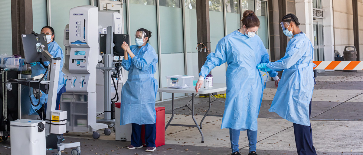 People in blue hospital gowns wearing masks, standing next to equipment