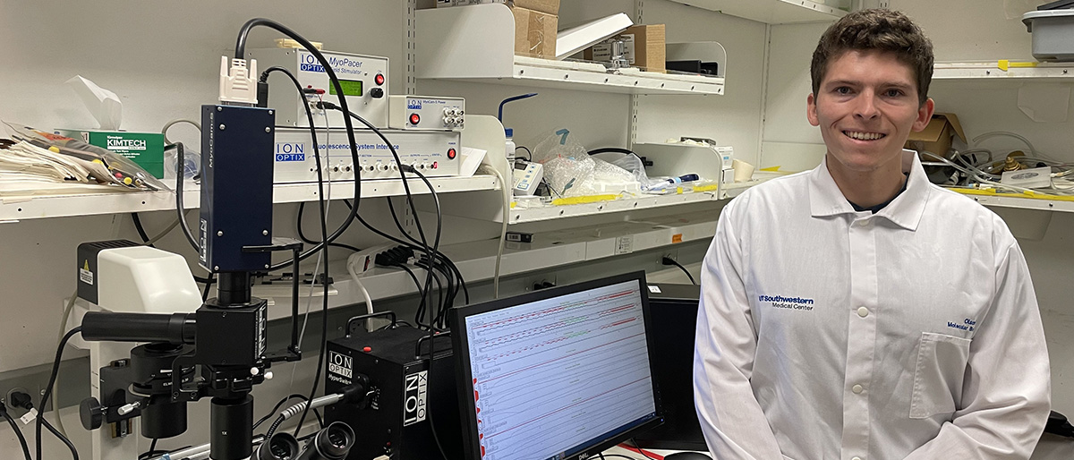 Smiling man with short dark hair wearing a white tee shirt, standing in a lab.