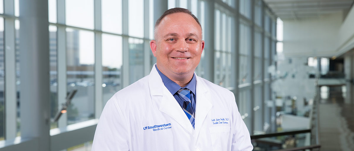 Man with short brown hair, wearing blue shirt and white lab coat