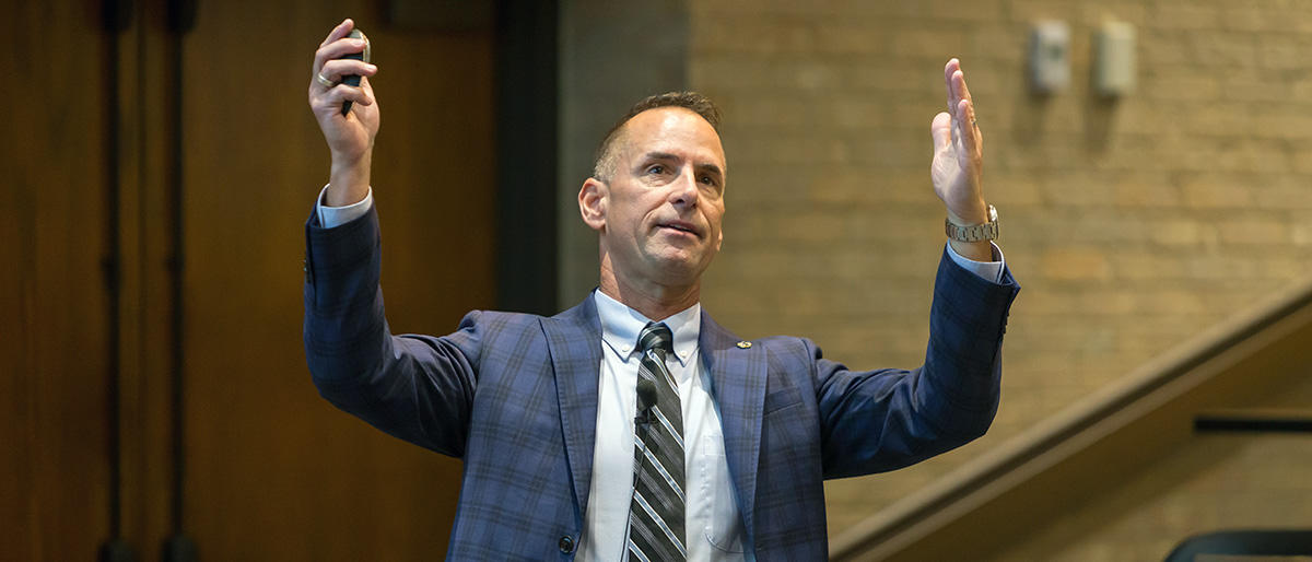 Man in blue and gray plaid suit with hands raised in the air.