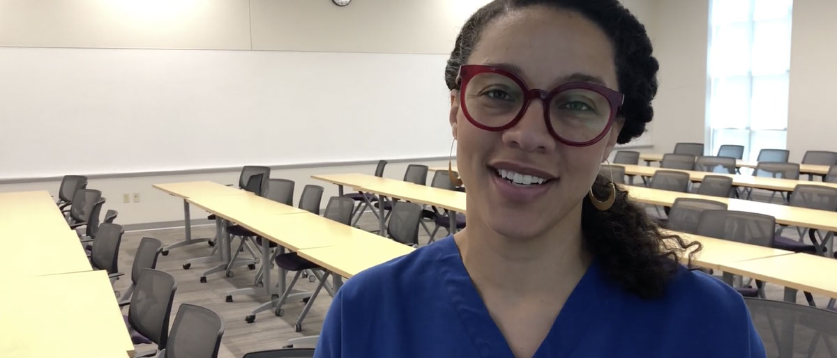 Woman in blue scrubs with red glasses standing in classroom