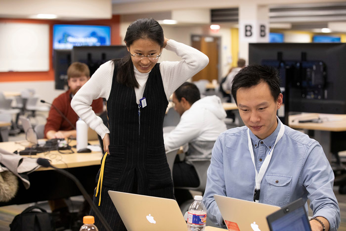 two people, one standing and the other sitting at a computer