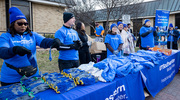 UTSW Office for Institutional Opportunity staff welcome volunteers to their table at the outdoor event, offering T-shirts, gloves, hats, and hand warmers.