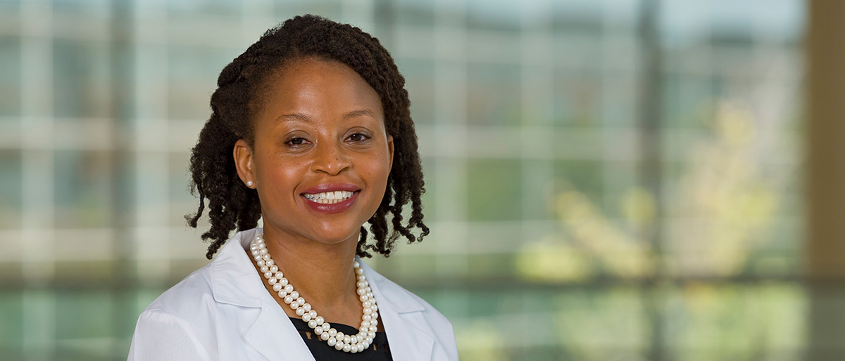 Smiling woman with dark hair wearing a white lab coat with beads around her neck.