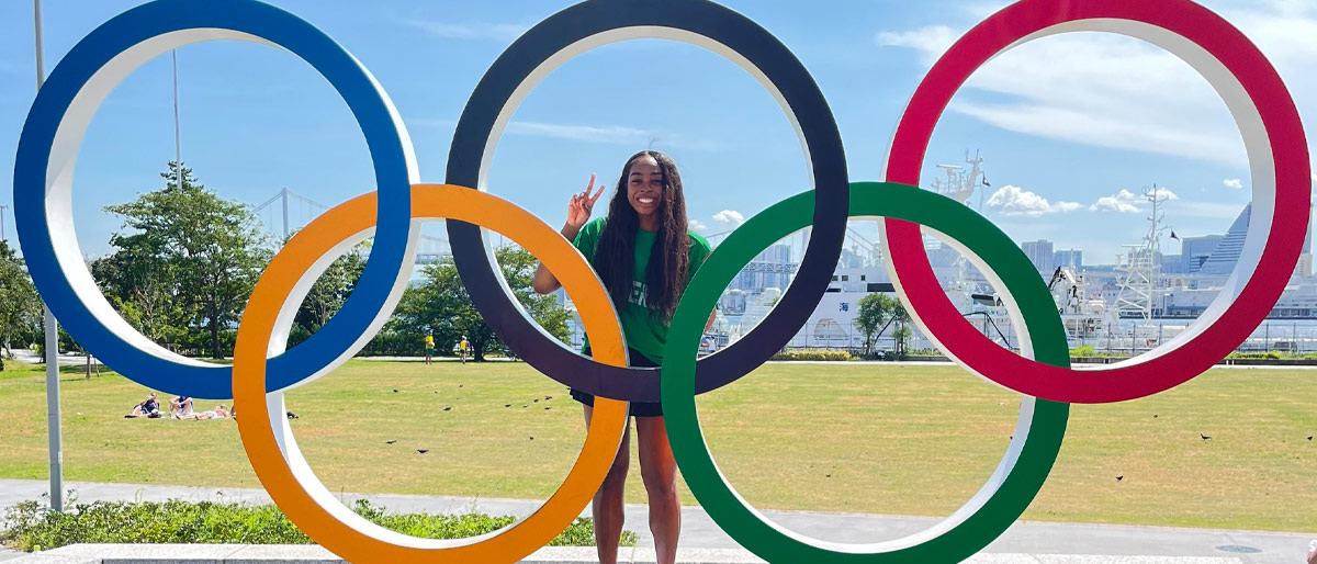 Woman standing behind large statue of 5 colored rings