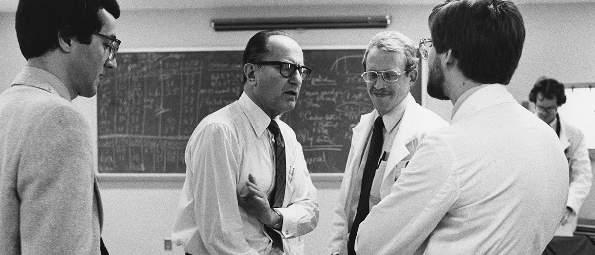 man talking to students in white lab coats