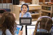 A student raises his hand in excitement to answer a question. The school incorporates the latest in technology, including interactive touch-screen lessons.