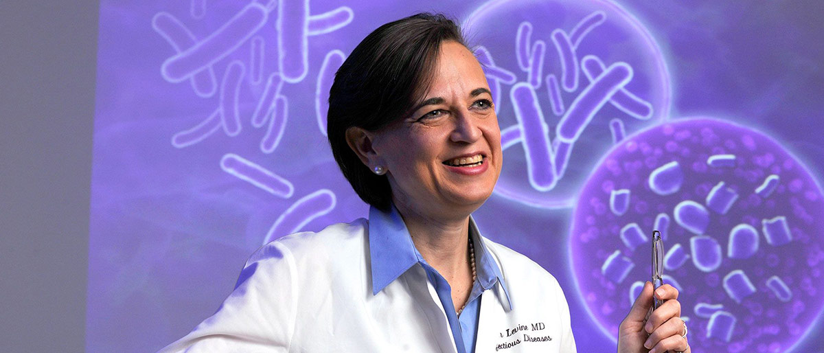 Woman in white lab coat in front of displayed slide, smiling and talking