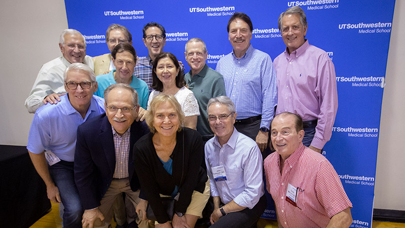 Group of people smiling and posing in front of a UTSW background for a photo