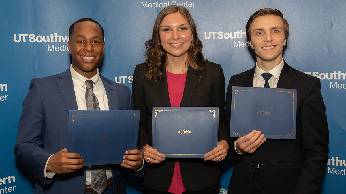 Three people holding folio awards and smiling