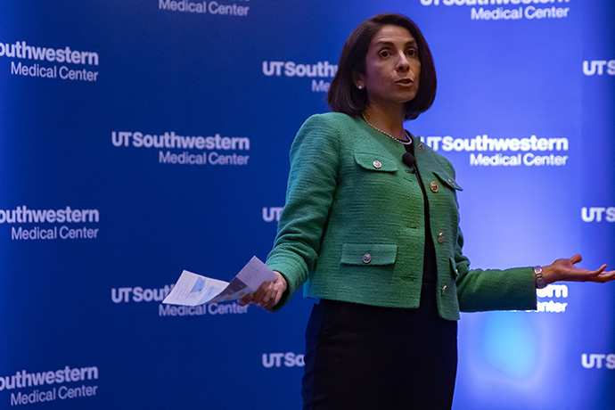 dark haired woman with green blazer speaks on stage at UTSW