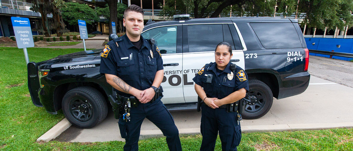 Two uniformed officers in front of a UT police vehicle