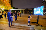 Dr. Aditya Bagrodia watches as his children point out his video montage on the monitors on the plaza.