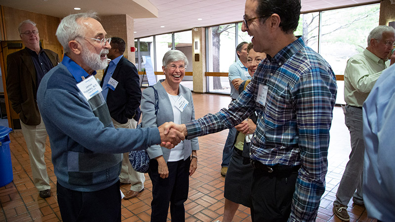 A younger and older man shaking hands and smiling