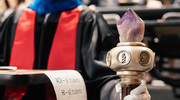 A faculty member holds the Stembridge Mace that is carried during the academic procession. The symbol represents the torch of learning and the passing of knowledge from teacher to student over generations.