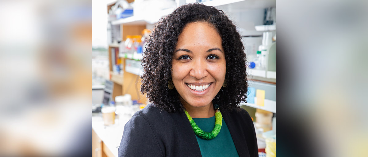 Smiling woman with dark jacket and green dress in a lab