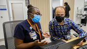 Kenya Lewis (left), a Workflow Analyst, confers with Dr. Humza Siddiqi in a patient care area.