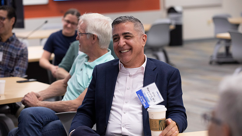 Man seated a table holding coffee and smiling