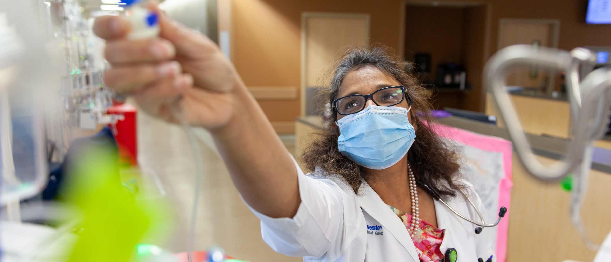 Woman in lab coat and face mask in hospital reaching up and adjusting valve