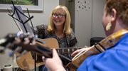Simmons Cancer Center music therapist Christina Shocklee, M.M.T., MT-BC, (facing backwards) conducts a music therapy session with cancer patient Sheryl Bennett (facing forward), who plays along on her acoustic guitar. Music therapy has been shown to improve well-being during and after cancer treatment, according to Ms. Shocklee. Patients do not need to have a musical background to benefit from music therapy services.