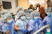Students gear up in hairnets and surgical gowns before entering the simulation OR room.