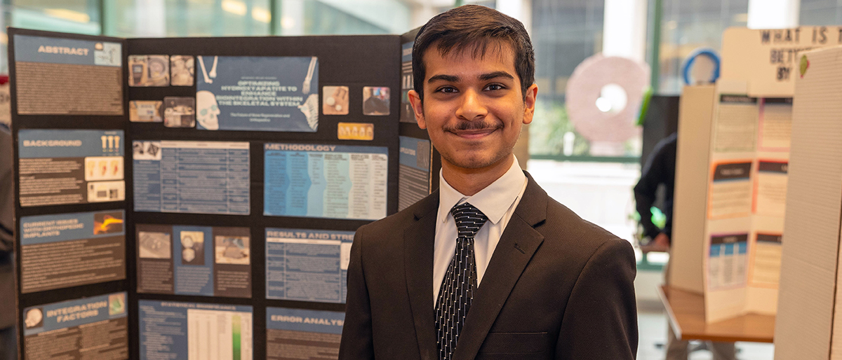 Student standing by his science fair poster.