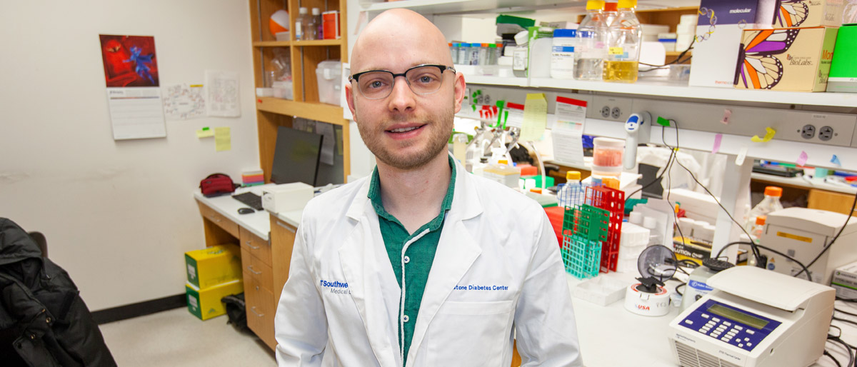 Man with shaved head, glasses, wearing lab coat in lab