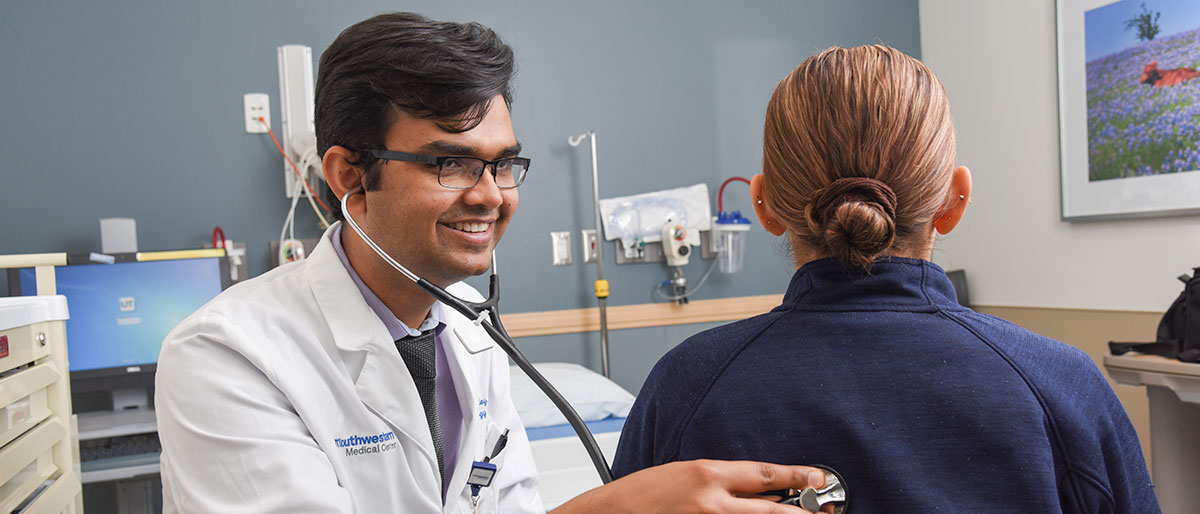 Man in white lab coat using stethoscope on person