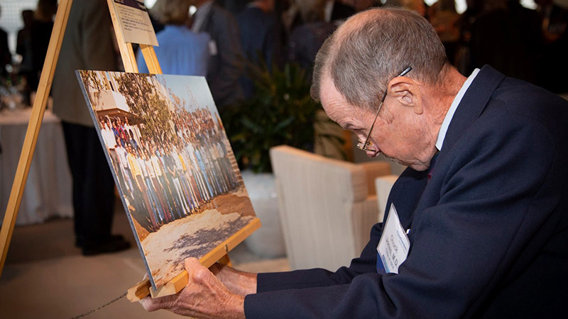 Man peers over glasses at a photo fo a group of people