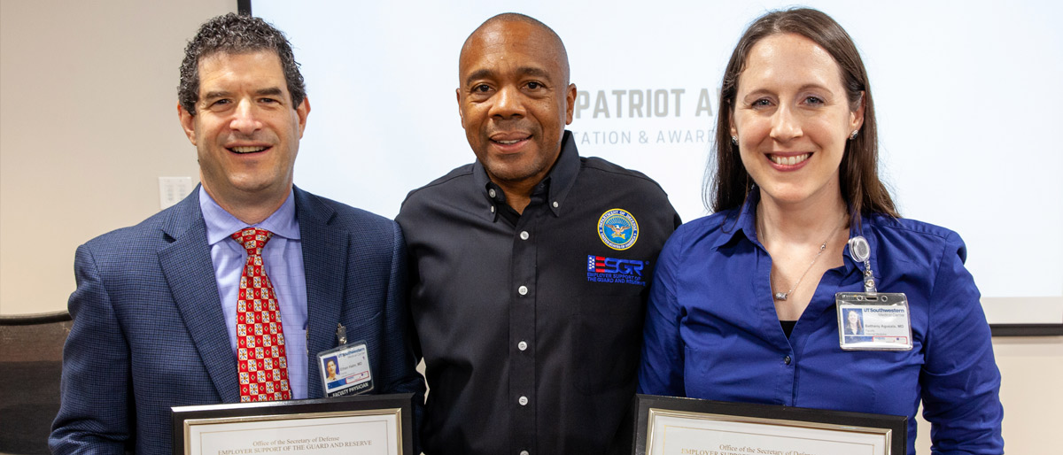 Three people standing side by side, the two on the sides holding awards