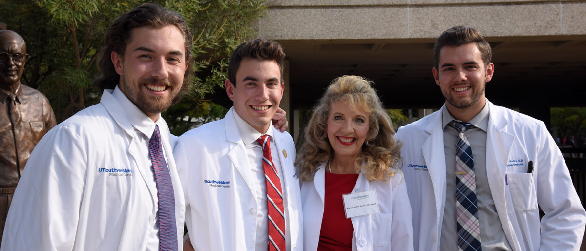 Group of four people, three younger men and one older woman, all in white lab coats