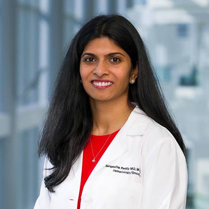 woman with long dark hair in white lab coat and red blouse