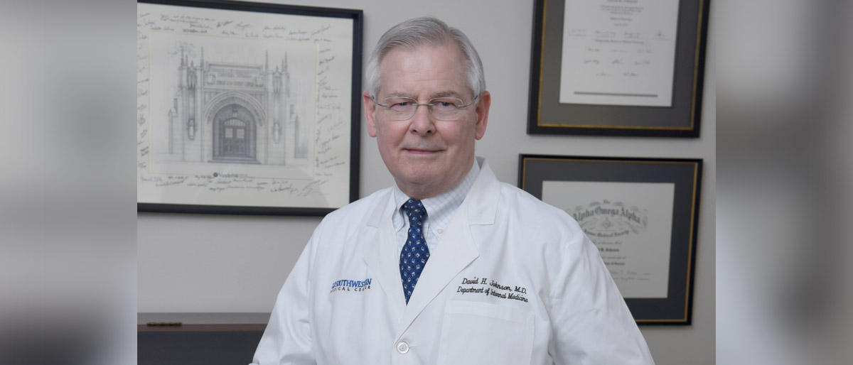 Man in lab coat standing in front of framed degrees