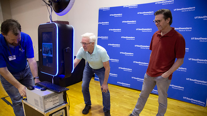 Two people standing in front of a photobooth camera with one person off to the side