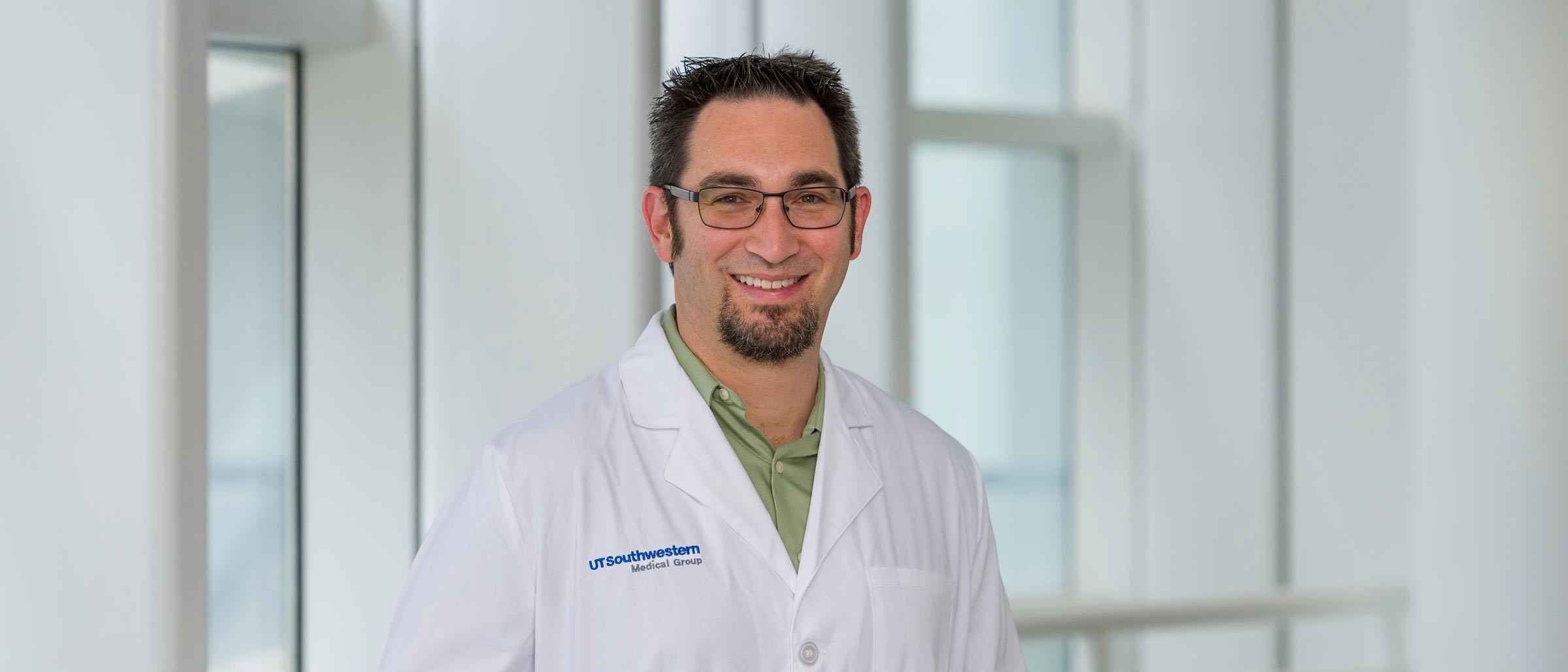 Man with black hair, glasses, goatee in white lab coat