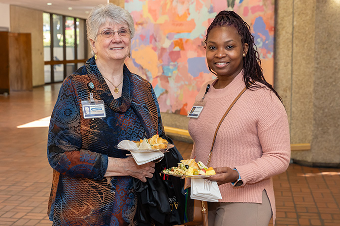 two women meet while sharing food, grey haired older woman on left, young black woman in pink sweater right