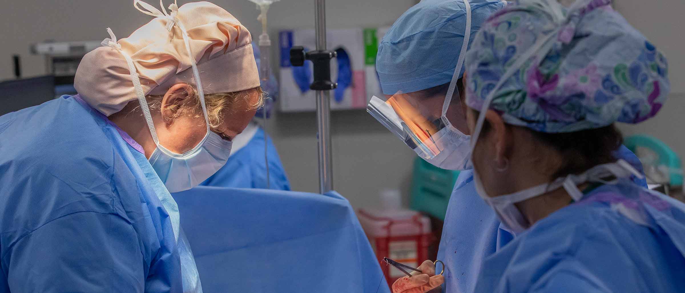 Three people in surgical scrubs performing surgery