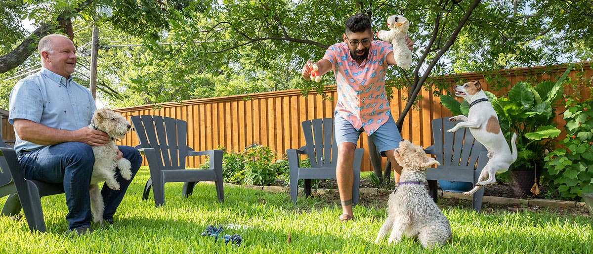 Two men in backyard playing with dogs