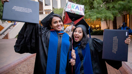 Two graduates in black robes smiling and holding their diplomas