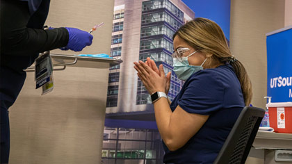 Woman in mask and scrubs clasping hands in excitement