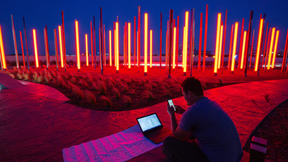 Night time photo of multi-colored glowing narrow tubes rising up from the ground.