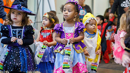 A group of young children wearing Halloween costumes, carrying their treat bags.