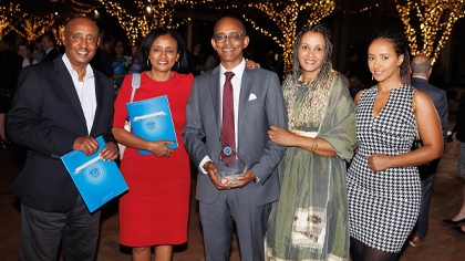 Family and friends (4) pose with one of the winners outside in front of trees draped with twinkle lights.