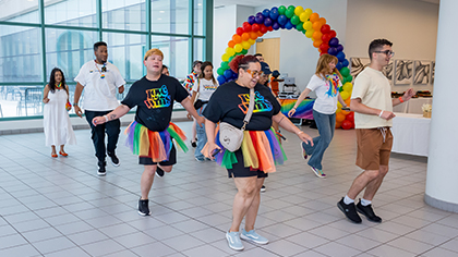 Participants practice line dancing in front of a rainbow balloon arch.