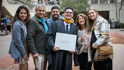 Family and friends (5) stand beind a young graduate holding his new diploma.